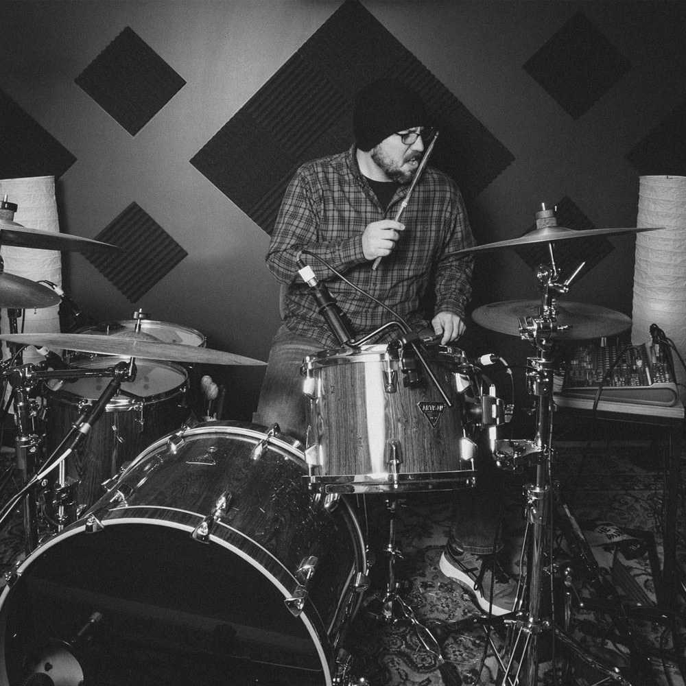 Miguel Monroy playing drums in a studio, photographed in black and white.