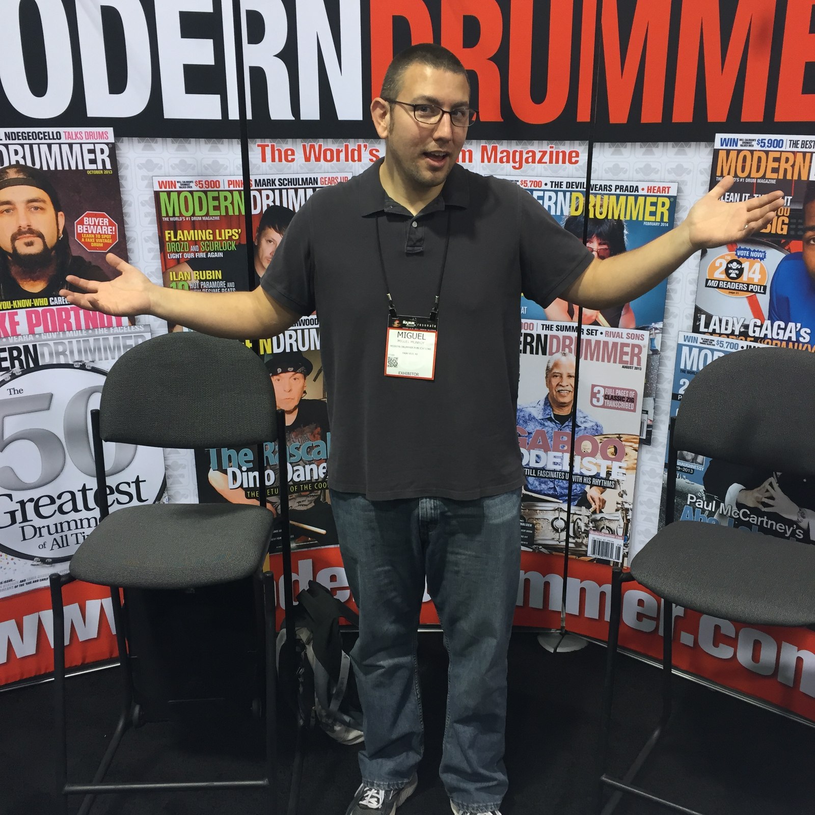 Miguel at the Modern Drummer booth with his arms outstretched in front of magazine covers.